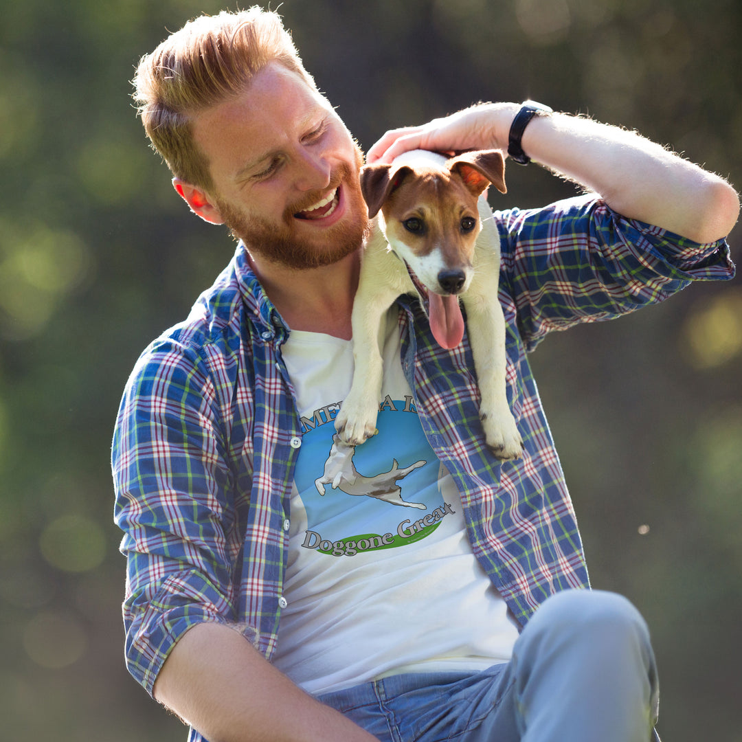 Man wearing an America is beautiful 'doggone' graphic shirt and holding a small dog outdoors with a blurred natural background