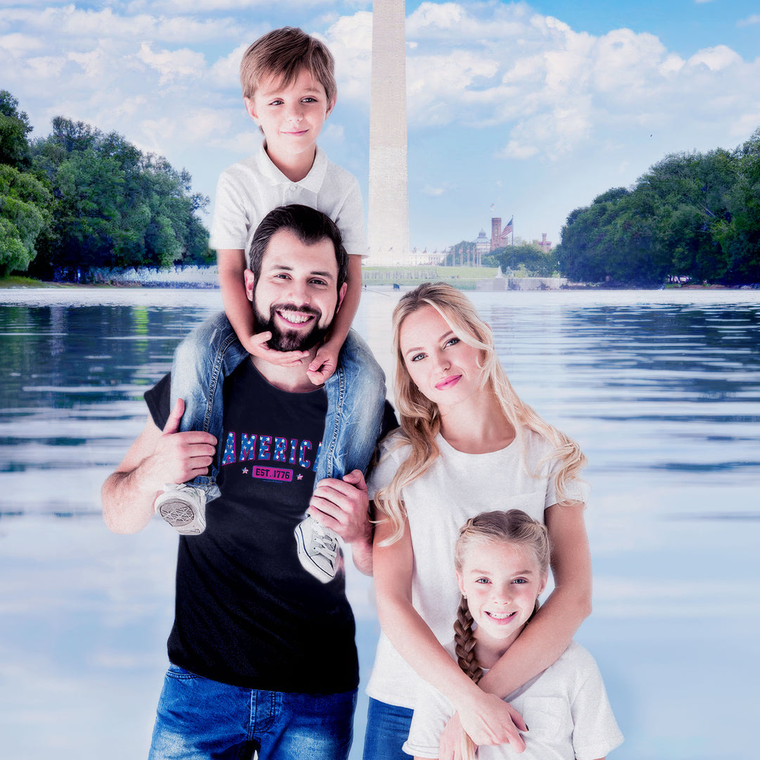 A family of four posing together in front of a Washington Monument backdrop. The father wears a Black t-shirt by America The Beautiful with 'AMERICA EST. 1776' text design