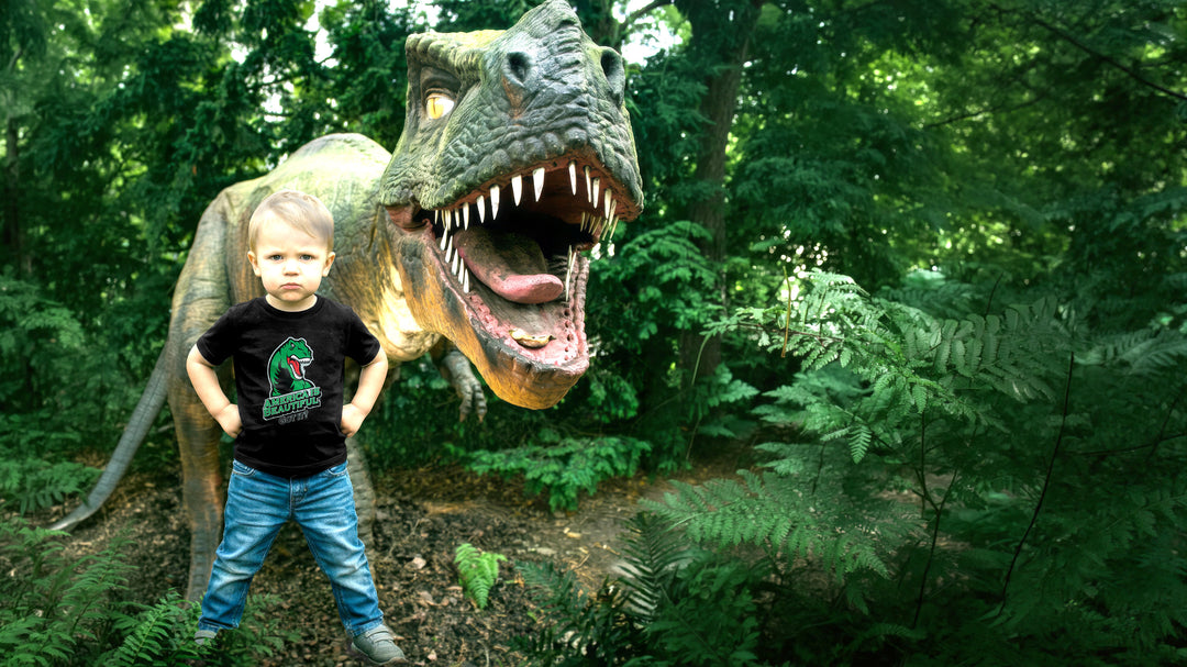 Child wearing a black t-shirt with a T-rex dinosaur graphic in front of a large dinosaur statue.
