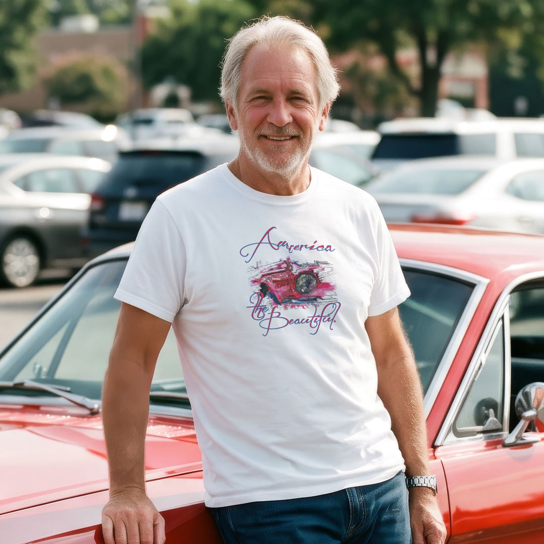 A smiling older man stands outdoors in front of a red 66 Mustang, wearing a white graphic T-shirt with a vintage Mustang headlight design and &