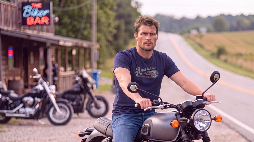 A man riding a motorcycle on a country road, wearing a Navy blue t-shirt with &