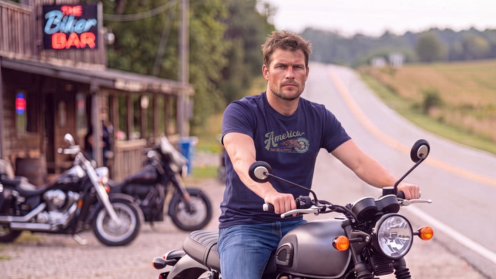 A man riding a motorcycle on a country road, wearing a Navy blue t-shirt with &