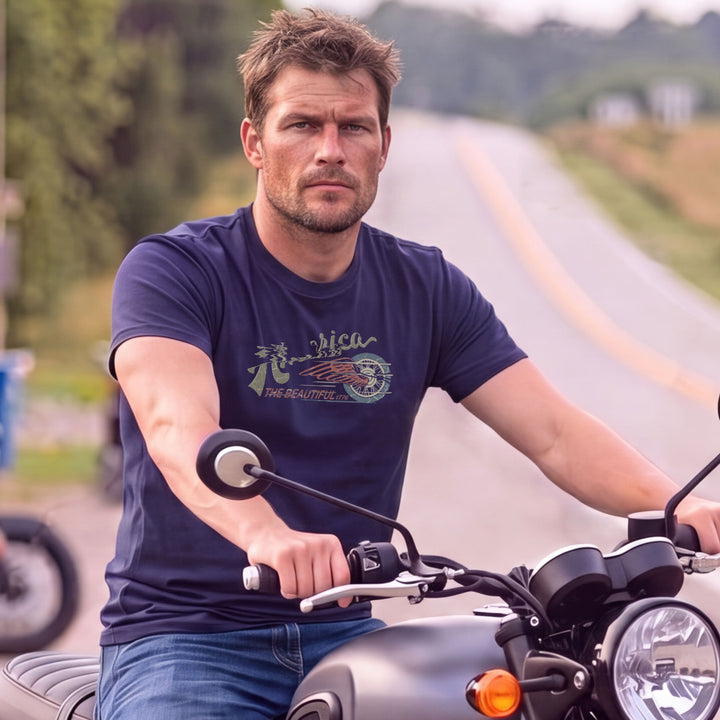 A man riding a motorcycle on a country road, wearing a Navy blue t-shirt with &