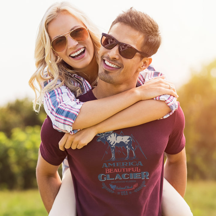 Man carrying a woman in a field, both wearing sunglasses, with a scenic background.