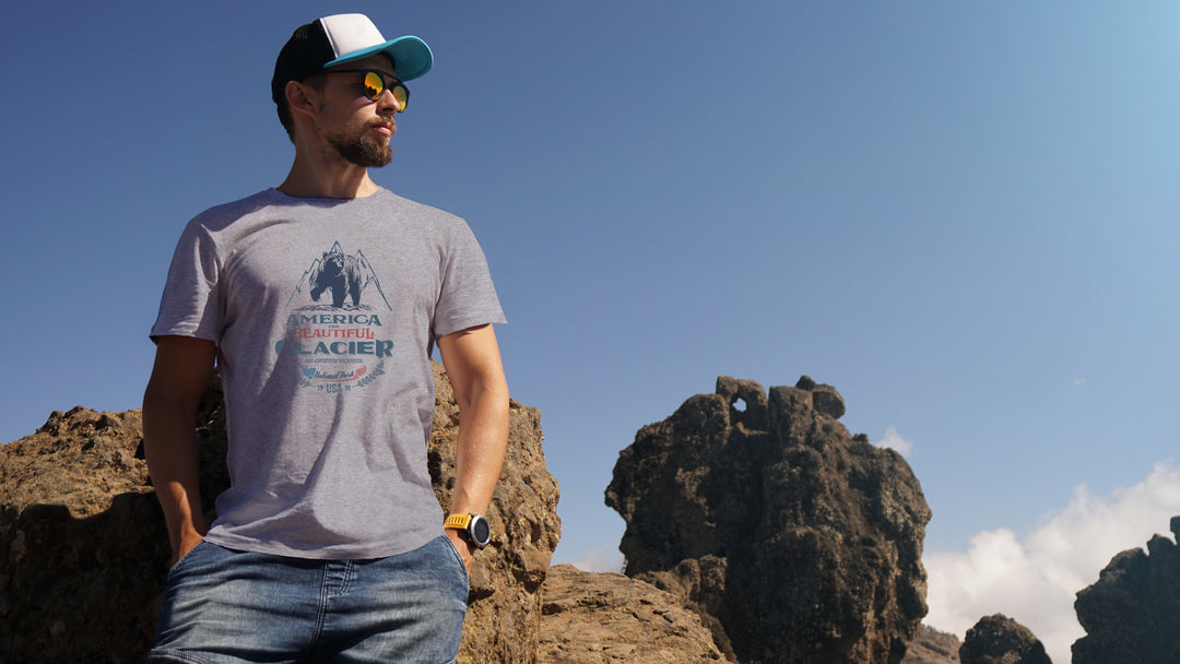 Man wearing a gray America The beautiful t-shirt with a Glacier Park Grizzly Bear outdoors against a clear blue sky.