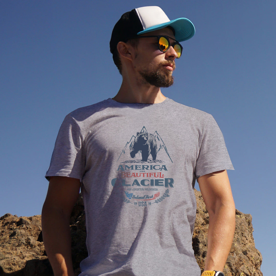 Man wearing a gray America The beautiful t-shirt with a Glacier Park Grizzly Bear outdoors against a clear blue sky.
