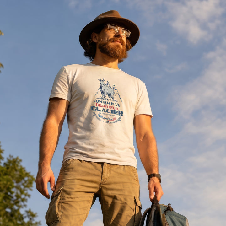 Man wearing a White t-shirt with graphic design featuring a Glacier Nat. Park mountain goat, standing outdoors against a blue sky.