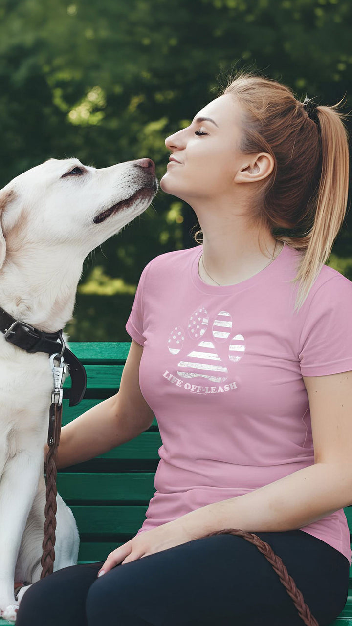 Woman sitting on a green bench with a white dog, both looking at each other outdoors.