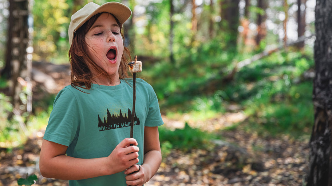 Child roasting a marshmallow wearing a Teal Magical Forest t-shirt with &