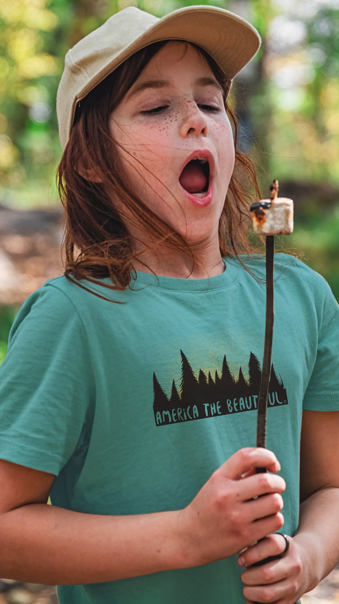 Child roasting a marshmallow wearing a Teal Magical Forest t-shirt with &