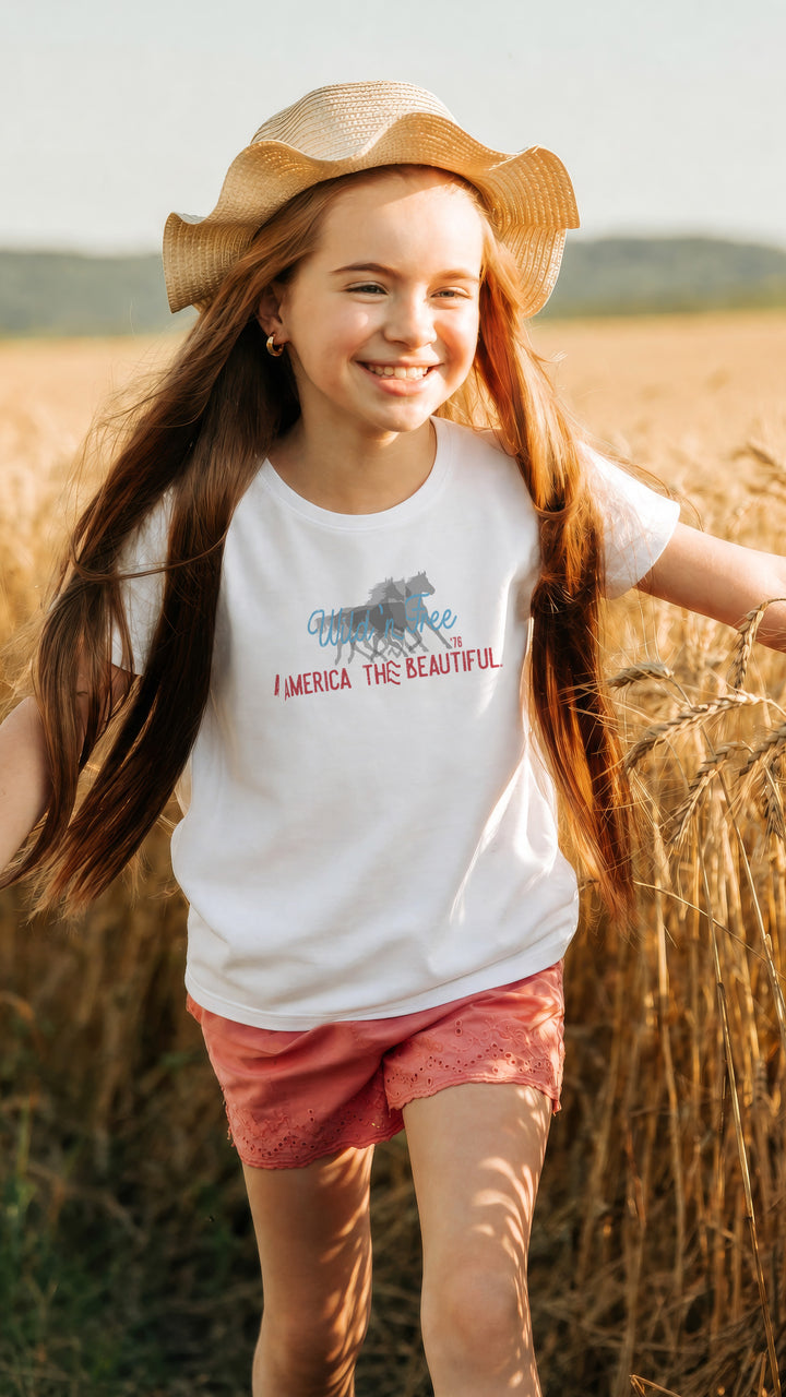 Smiling wild and free Young girl in a field wearing a White t-shirt with wild horses graphic design and America the beautiful text on a white background