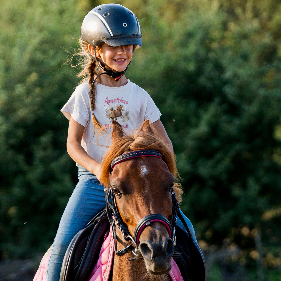 Girl riding horse wearing White t-shirt with horse graphic and 'America the Beautiful' text 
