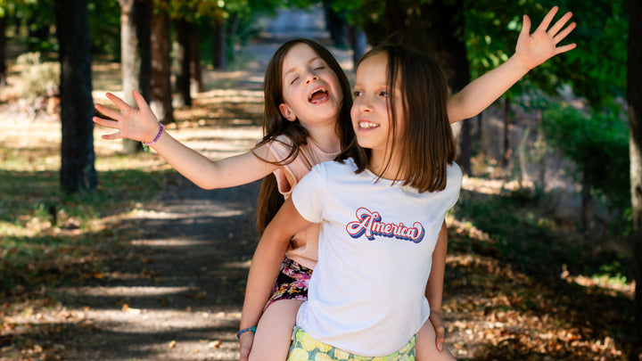 Two young girls playing outdoors with trees in the background and our "America" shirt