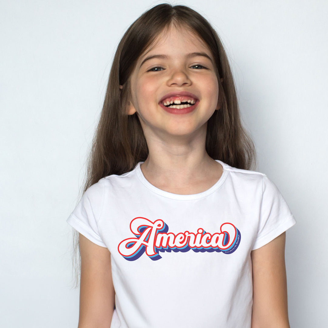 Young girl wearing a white t-shirt with 'America' printed on it against a plain background